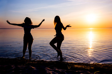 Two beautiful girls, students are dancing on the beach at sunset background
