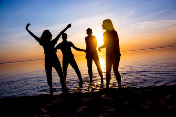 Young people, guys and girls, students are dancing on the beach at sunset background, silhouettes