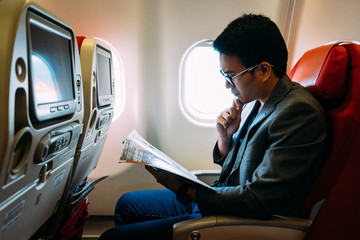 Young asian business man smiling and reading a book in airplane