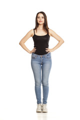 young woman in jeans and shirt stands on a white background