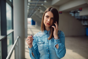 Young casual dressed brunette watching through window while having phone call