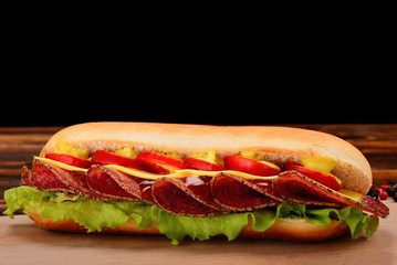 Sandwich with salami, cheese, cherry tomatoes, lettuce and mustard on a black background. Space for text or design.