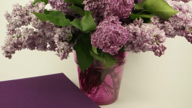 A bouquet of lilacs in a vase and a book on a white background