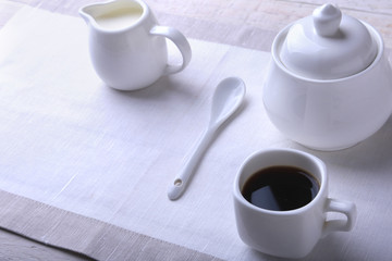 Cup of hot coffee espresso, coffee beans, jug of milk, and bowl with sugar on white background for copy space. Coffee concept.