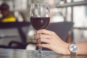 a glass of red wine in a female hand. The girl in the restaurant drinks wine