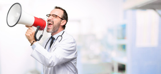 Doctor senior man, medical professional communicates shouting loud holding a megaphone, expressing...
