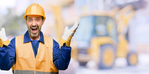 Senior engineer man, construction worker happy and surprised cheering expressing wow gesture at work - obrazy, fototapety, plakaty