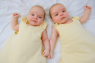 Two adorable twin babies lying down on white sheet in yellow sleeping sacks ready to go to bed. Safe sleep for babies. Infants in wearable blankets