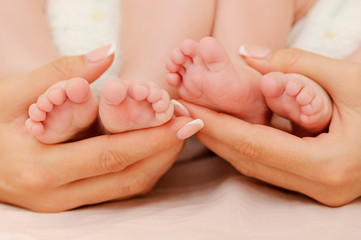 Fototapeta na wymiar Mother holding tiny feet of her twin babies. New life and family values. Love and tenderness