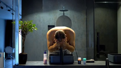 Young man washing face in bathroom
