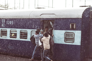 Crowd boarding train in Haridwar railway station under heavy monsoon rain. Young boys fighting to get on the coach.
