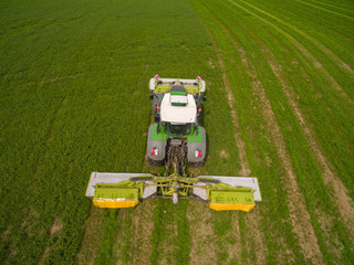 Aerial view of a tractor mowing a green fresh grass field, 
a farmer in a modern tractor mowing a green fresh grass field on a sunny day