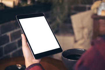 Mockup image of hands holding black tablet pc with white blank screen and coffee cup in cafe