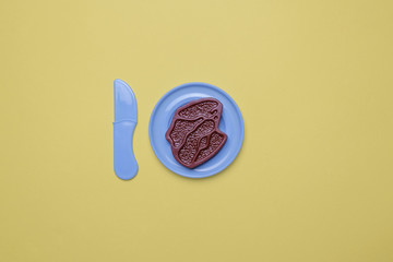 Toy Plastic Steak with Knife on a Yellow Background