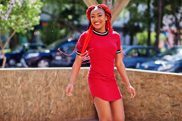 Cute and slim african american girl in red dress with dreadlocks in motion having fun on street. Stylish black model.