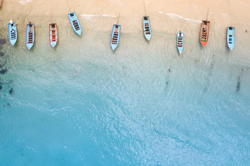 Aerial: Shoreline with thai long tail fishing and taxi boats parking along the sand beach of...