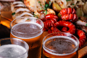 Three glasses of beer near the set of grilled meat on wood backr