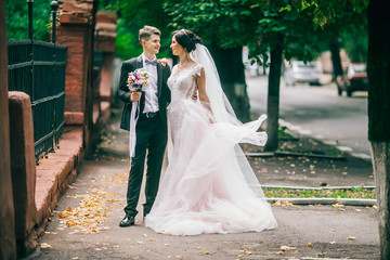Naklejka premium A loving couple of newlyweds walks in the city. Husband and wife on a walk. Bride and groom hug and kiss each othe at athe street. Adorable couple.