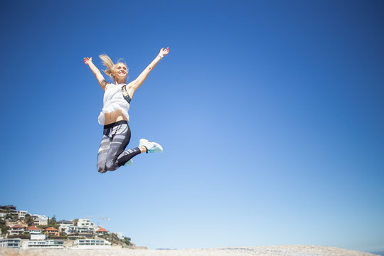 Beautiful blond female fitness model jumping from one rock to another on a bright sunny day