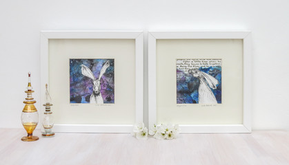 White interior display. Two drawings of hares on collaged blue backgrounds in frames. With egyptian...