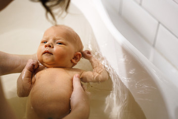 The newborn swims in the bathroom in the arms of the mother. The first bathing of the baby in the bathroom.