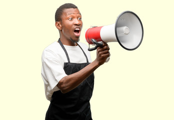 African man shop owner wearing apron communicates shouting loud holding a megaphone, expressing success and positive concept, idea for marketing or sales