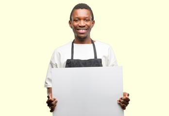 African man shop owner wearing apron holding blank advertising banner, good poster for ad, offer or announcement, big paper billboard