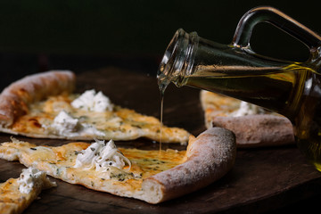 Olive oil puring on Quattro formaggi pizza on wood background