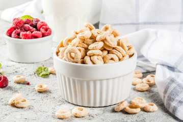 Healthy breakfast ingredients. Breakfast cereal corn rings, milk or yogurt glass, raspberries and mint on grey stone background, copy space