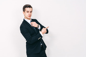 Portrait of a young happy  businessman in suit pointing finger away over white background