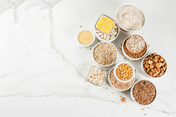 Selection various types cereal grains groats  in different bowl on white marble background, copy space above