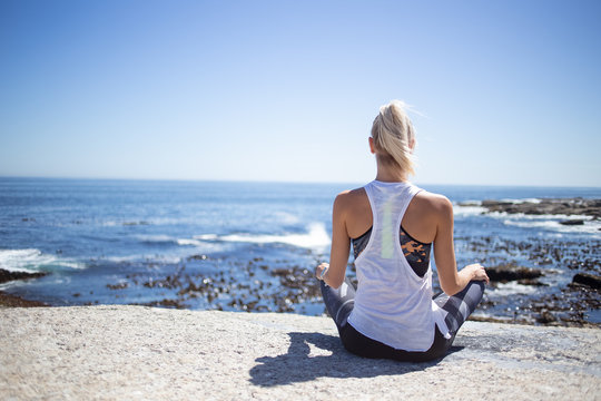 Blond female fitness model meditating and doing yoga on a granite rock overlooking the ocean