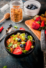 Healthy breakfast with muesli or granola with nuts and fresh berries and fruits - strawberry, blueberry, kiwi, on dark blue table, copy space