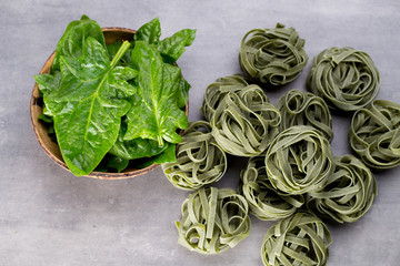 Fresh spinach with green pasta on a gray background.