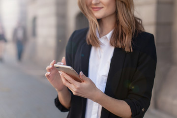 Cropped shot of young girl using modern smartphone device, female hands holding mobile phone on city street, smiling successful female entrepreneur using cellphone wireless connection for work outside