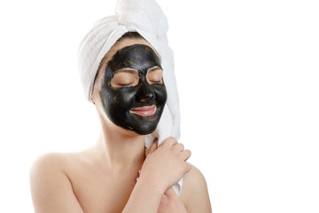  close-up portrait beautiful woman with facial black mask on white background, girl with a white towel on her head, satisfied and happy closed eyes