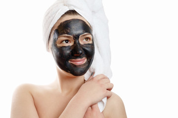  close-up portrait beautiful woman with facial black mask on white background, girl with a white towel on her head, satisfied and happy  smile
