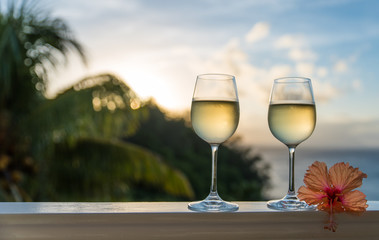 Romantic moments in summer at sunset with two glasses of white wine - Relaxing romantic holiday concept with beautiful view of tropical beach and coast