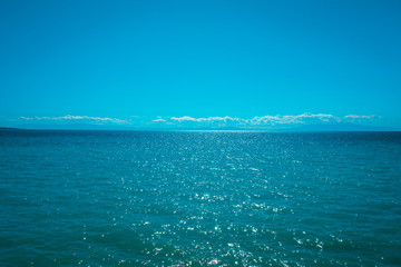 blue sea with small fluffy clouds in the background