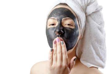  close-up portrait beautiful woman with facial black mask on white background, girl with a white towel on her head, satisfied and happy  smile, air kiss