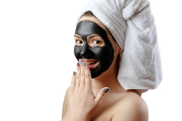  close-up portrait beautiful woman with facial black mask on white background, girl with a white towel on her head, satisfied and happy  smile, covers a laugh with his hand