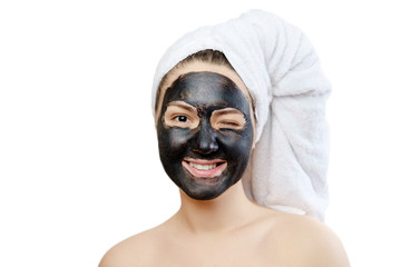 close-up portrait funny beautiful woman with facial black mask on white background, girl with a white towel on her head, satisfied and happy  smile in the camera