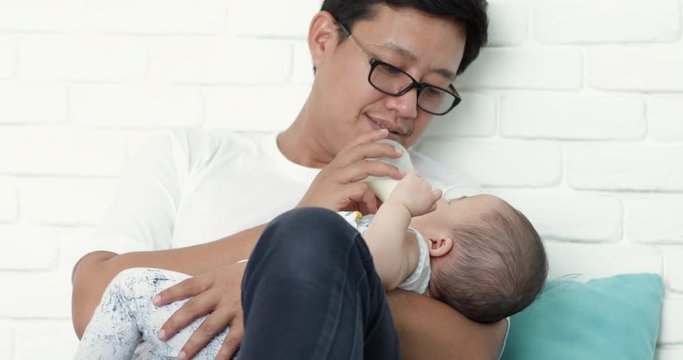 Young asian  father feeding her baby girl milk formula from a bottle in the living room
