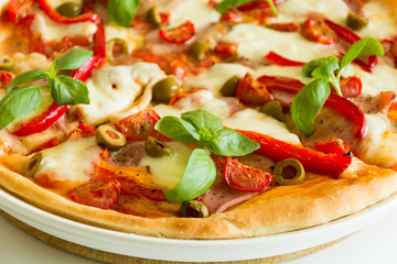 Fresh pizza with tomatoes, cheese mozzarella, red pepper and olives decorated basil leaves on white wooden table. Close up
