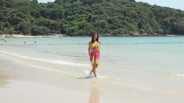 The girl runs on the sandy beach. It is developed to the camera, smiles and waves a hand.