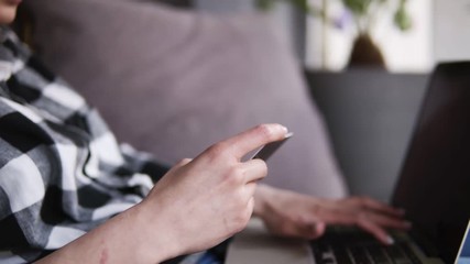 The girl typing numbers from the card to the computer. Successfully finished, she continues to type on the laptop. Sitting on the couch. At home. Move away shooting
