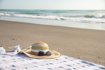 Hat on a blanket on sandy beach with ocean wave in background