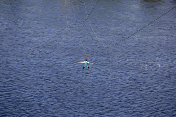Rear view of young man riding on zip line against a background of a blue river water wave