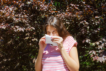 Front view of a single girl sneezing and blowing in a wipe outdoors with a green background
