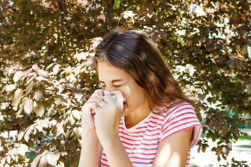 Fototapeta premium Young pretty girl blowing nose in front of tree. Spring allergy concept